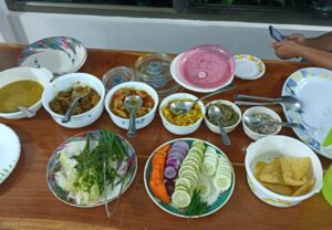 A colorful platter of traditional Meghalayan curries with fresh vegetables and rice, served on a wooden table in the Sarangdu Homestay dining room.